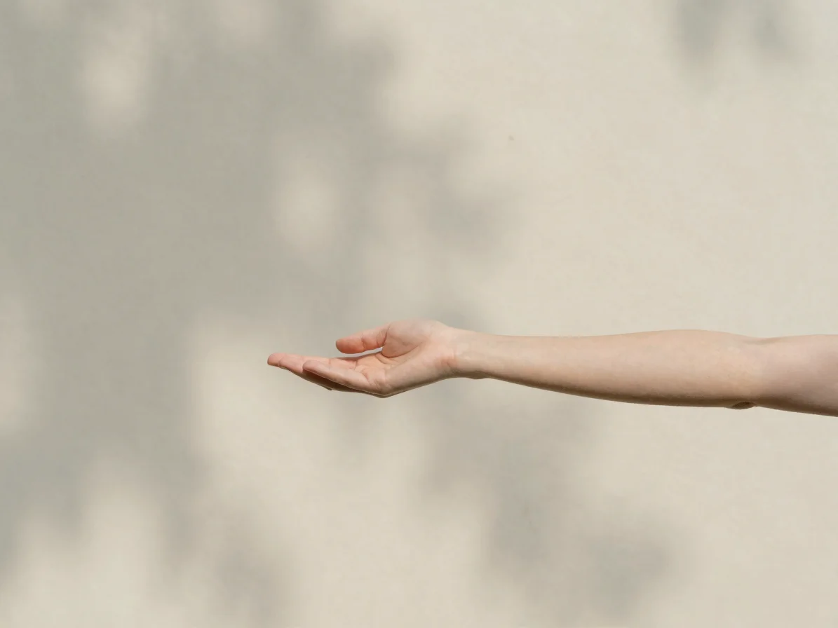 Natural editorial photograph of a person gently stretching arms outdoors in soft open-shade daylight, unposed, ivory sag